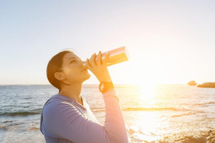 women sips water on a beach at sunset